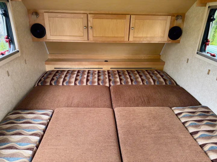 Cozy RV rental interior featuring a comfy bed with patterned cushions, wood cabinets, and windows.. Pleasant Valley/NuCamp T@B 2016