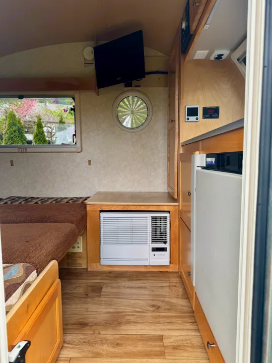 Spacious RV rental interior featuring a comfortable bed, multiple windows, mounted TV, AC unit, and refrigerator.. Pleasant Valley/NuCamp T@B 2016