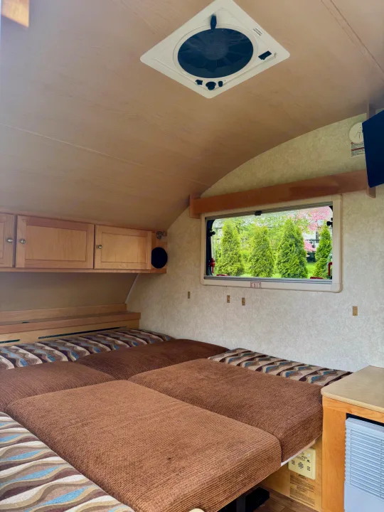 Cozy RV rental interior featuring a comfortable bed, overhead cabinets, and a scenic window view.. Pleasant Valley/NuCamp T@B 2016