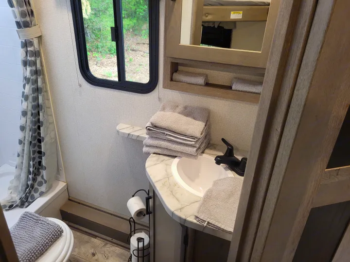 Compact RV rental bathroom with a shower, sink, toilet, window, and neatly folded towels, maximizing space.. Keystone Outback 2021