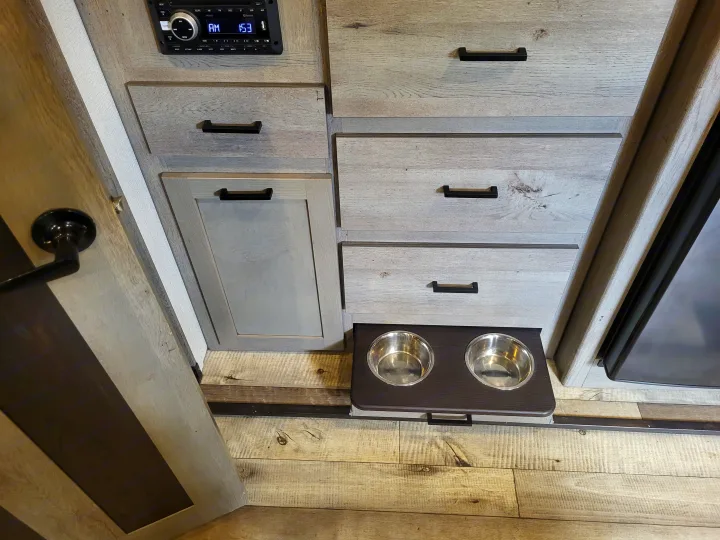 Modern RV rental interior featuring an integrated pull-out pet food station, a media player, and sleek storage cabinets.. Keystone Outback 2021