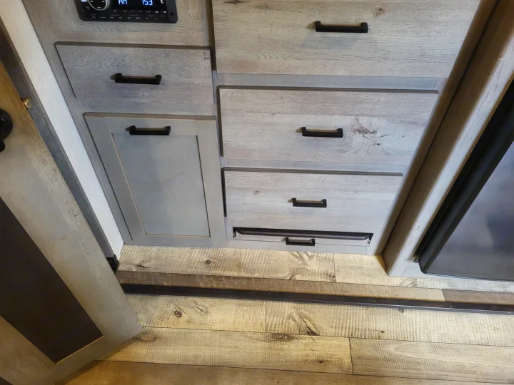 RV rental interior with light wood-look cabinetry, black handles, a control panel, and textured laminate flooring, showing storage.. Keystone Outback 2021