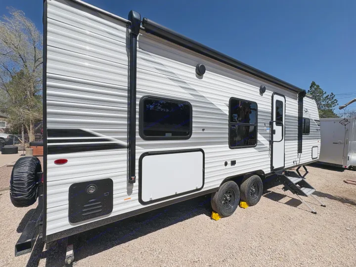 This white & gray travel trailer for RV rental, with an awning and windows, is parked on a gravel lot.. Jay Flight SLC 260BHW 2025