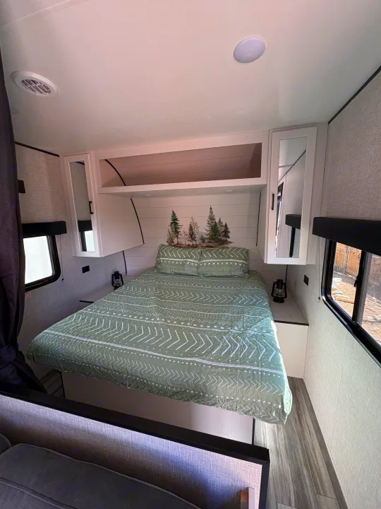 RV rental bedroom with a green patterned bed, forest wall art, white cabinets, and bright windows, offering a cozy space.. Jay Flight SLC 260BHW 2025