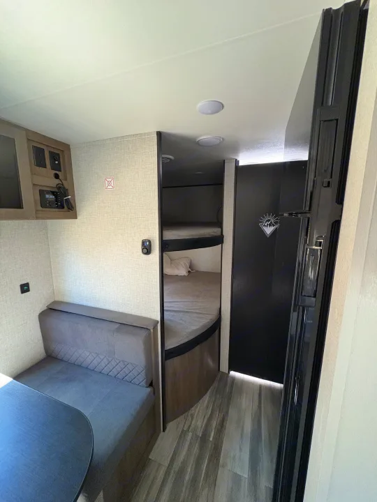 Inside this RV rental: dinette with table & bench, entertainment system, bunk beds, and a dark refrigerator. Wood floors.. Jay Flight SLC 260BHW 2025