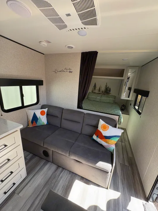 Bright rv rental interior featuring a convertible gray sofa, full bed nook, light wood floors, and modern decor.. Jay Flight SLC 260BHW 2025