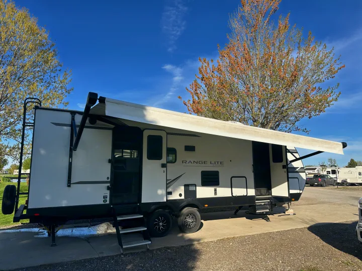 A white and black RV travel trailer, ideal for an RV rental, parked with its awning extended for a relaxing campsite stay.. Highland Ridge RV Open Range 2022