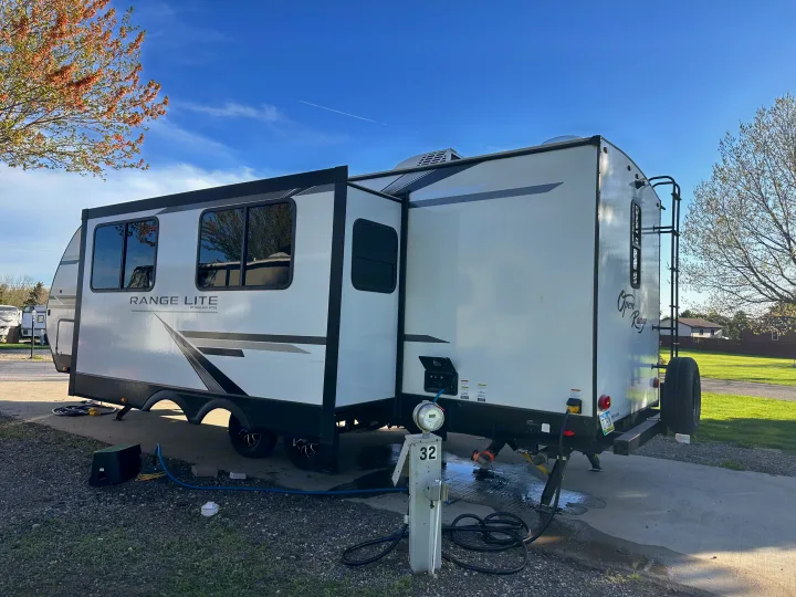 This white Range Lite travel trailer, an RV rental, is set up at campsite 32 with utilities connected, ready for camping.. Highland Ridge RV Open Range 2022