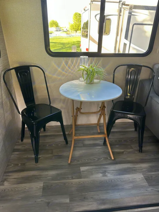 RV rental interior: A cozy dining area features a white table, two black chairs, and a plant, with a sunny window view.. Highland Ridge RV Open Range 2022