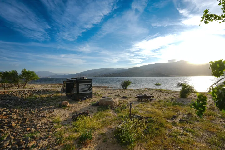 RV rental parked at a serene lakeside campsite, with mountains in the distance and a beautiful sunset glow.. Thor Delano Sprinter 2020