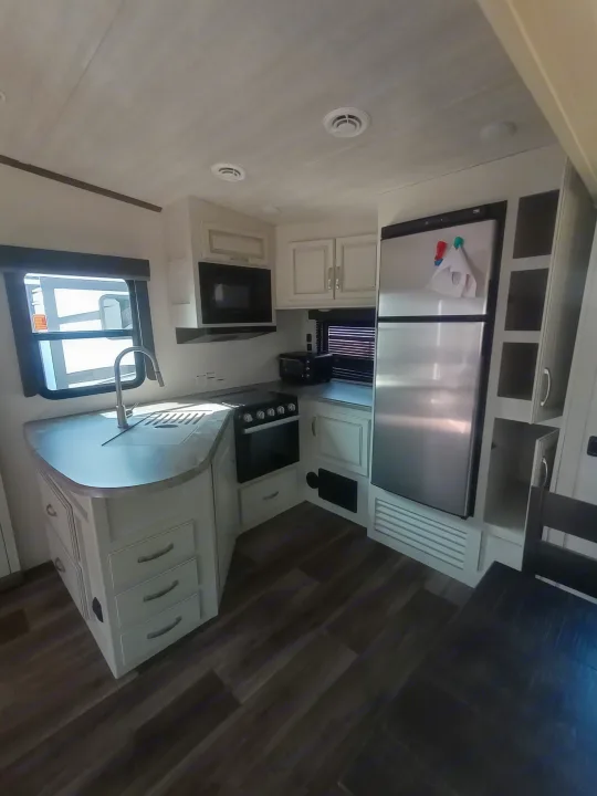 Modern RV rental kitchen featuring light cabinets, dark counters, stainless appliances, and wood-look flooring.. Keystone RV Cougar 2022