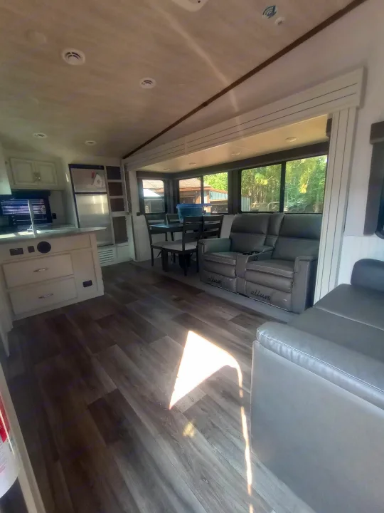 Spacious RV rental interior featuring a modern kitchen, dining area, and gray reclining sofas on dark wood floors.. Keystone RV Cougar 2022