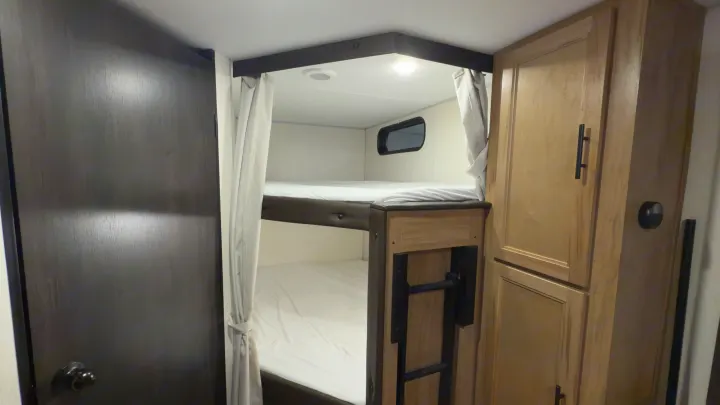 Cozy RV rental interior with comfortable bunk beds, storage cabinets, and privacy curtains, perfect for family adventures.. Forest River Grey Wolf 23DBH 2025