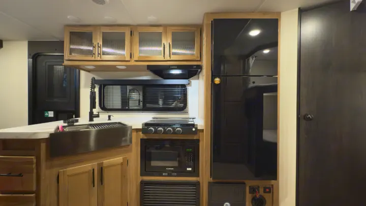 Modern RV rental kitchen with stainless steel sink, stove, microwave, and refrigerator, ideal for travel trailer adventures.. Forest River Grey Wolf 23DBH 2025