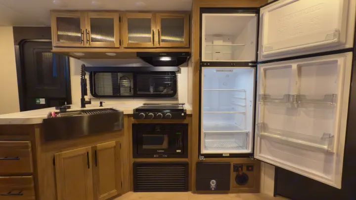 Modern RV rental kitchen with light wood cabinets, stainless sink, black appliances, and a large open refrigerator.. Forest River Grey Wolf 23DBH 2025