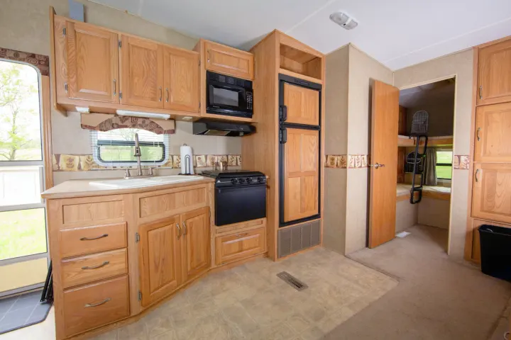 RV rental interior featuring a full kitchen with wooden cabinets, appliances, sink, and adjacent bunk beds.. Crossroads RV Cruiser 2006
