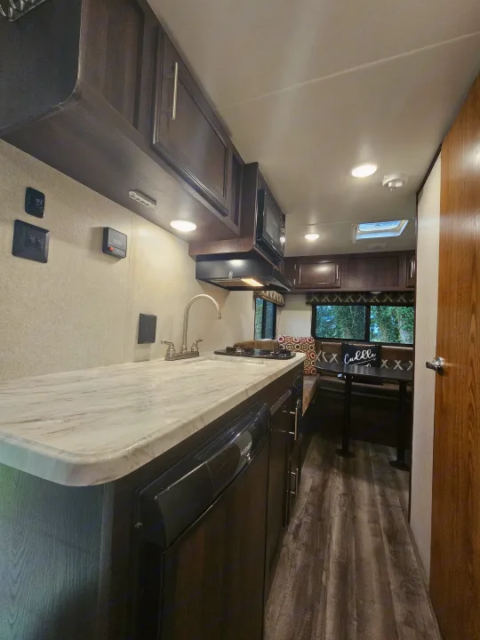 Interior of an RV rental showing a full kitchen with sink, stovetop, and appliances, leading to a cozy dinette area.. Jayco Jay Flight SLX 2019