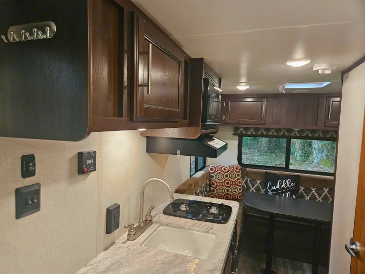 An RV rental's inviting interior: functional kitchen with sink & stove, rich wood cabinets, & cozy dinette by a large window.. Jayco Jay Flight SLX 2019