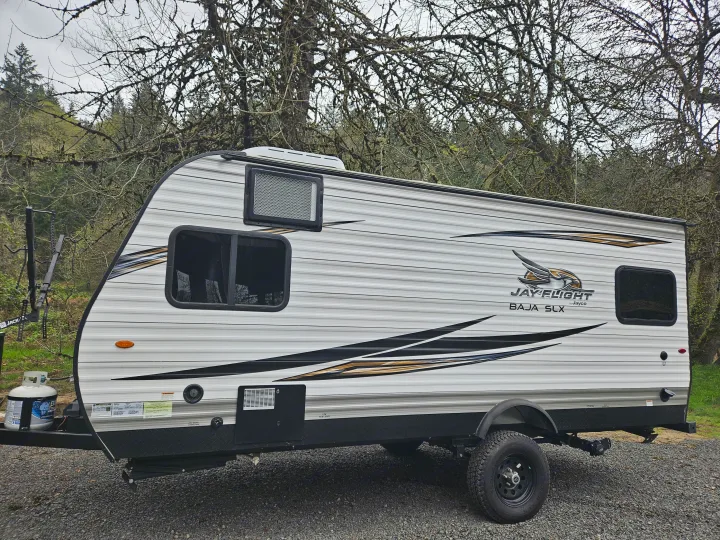 Explore nature with this Jayco Jay Flight Baja SLX rv rental, featuring off-road tires and a bike rack at a peaceful campsite.. Jayco Jay Flight SLX 2019