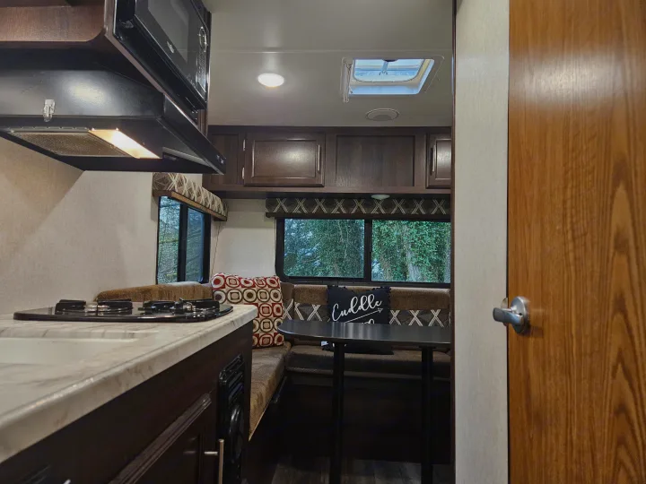 Cozy RV rental interior: kitchen with stovetop, dining booth with 'Cuddle' pillow, nature views from windows, and wood accents.. Jayco Jay Flight SLX 2019