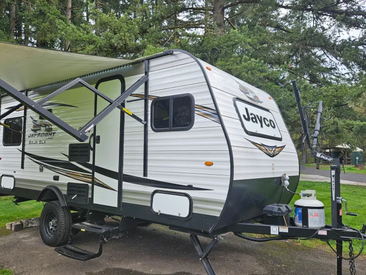White Jayco travel trailer rv rental with awning extended, parked at a wooded campsite with bike rack and propane tank.. Jayco Jay Flight SLX 2019