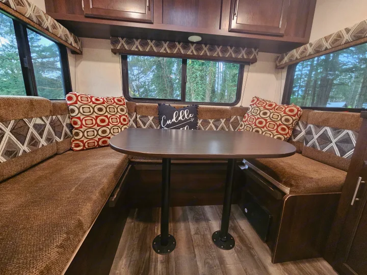 Cozy RV rental dinette features U-shaped booth seating, a dark table, patterned cushions, and windows with a view of trees.. Jayco Jay Flight SLX 2019
