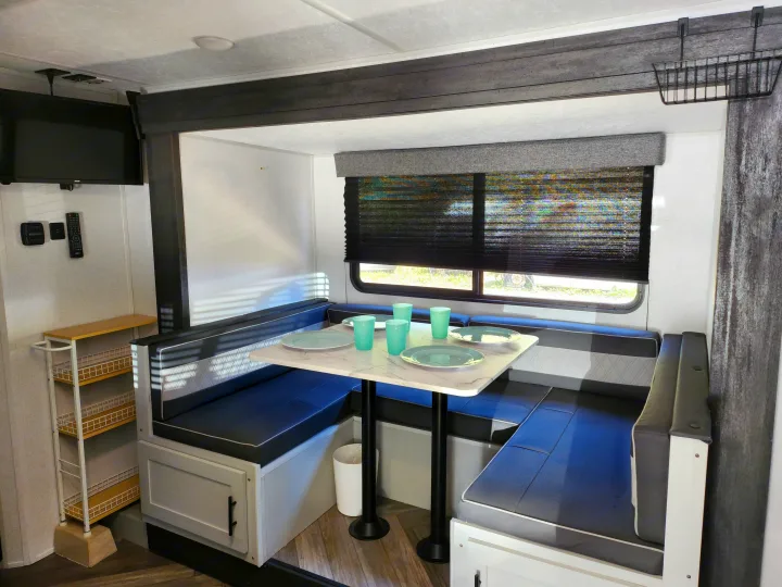 rv rental: Dinette area with a marble-look table, blue seating, privacy blinds on windows, wall TV, and side storage.. Forest River Wildwood FSX 2022