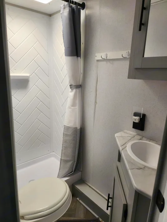 Compact RV rental bathroom with a white herringbone shower, toilet, and vanity sink. Modern interior for travel.. Forest River Wildwood FSX 2022
