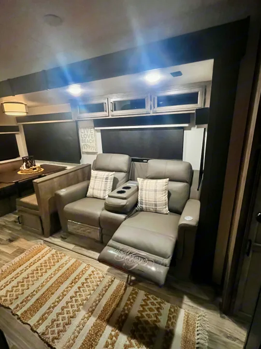 Modern RV rental interior: living area with gray reclining seats, cup holders, and footrest. Includes a dining booth.. Sporttrek Touring Edition 2024