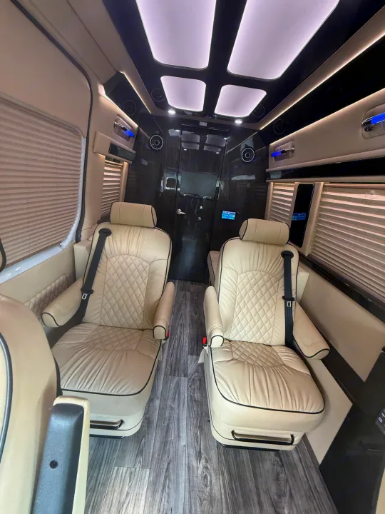 Luxurious RV rental interior: two cream, diamond-quilted captain's chairs, wood floor, and ambient lighting create a premium mobile lounge.. Ultimate Toys Ultimate Commuter 144 2022