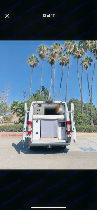 White camper van with open rear doors reveals custom interior bed and storage. Perfect rv rental for scenic camping trips.. Custom Ram Promaster 2021