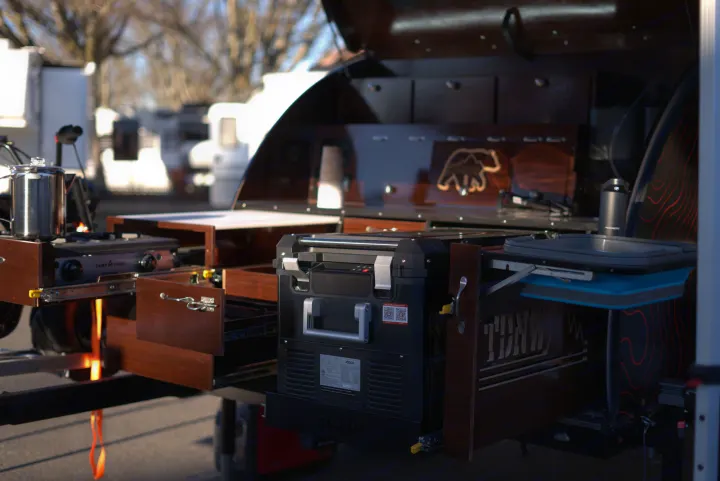 A custom outdoor kitchen in an RV rental, featuring a Camp Chef stove, fridge, pull-out wooden drawers, and bear decor.. Teardrops NW Ranger 2025