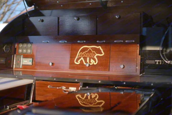 Detailed wooden cabinetry, a bear-mountain design, and an integrated power panel in an RV rental's interior.. Teardrops NW Ranger 2025