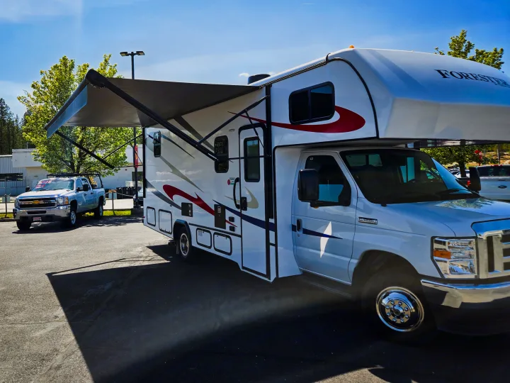 A white Forester Class C RV with an extended awning is parked outdoors on a sunny day, ready for rv rental.. Forester Classic 2022