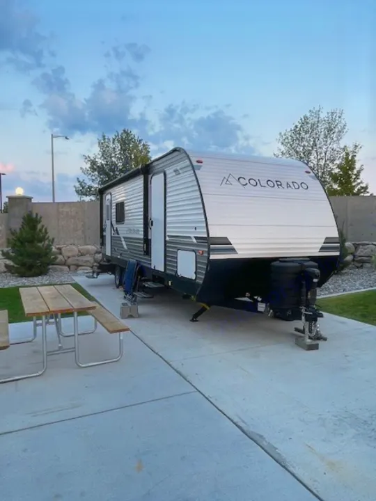 A 'Colorado' RV rental travel trailer parked on a concrete pad with a picnic table at a scenic campsite.. Dutchmen 23RKCWE 2024