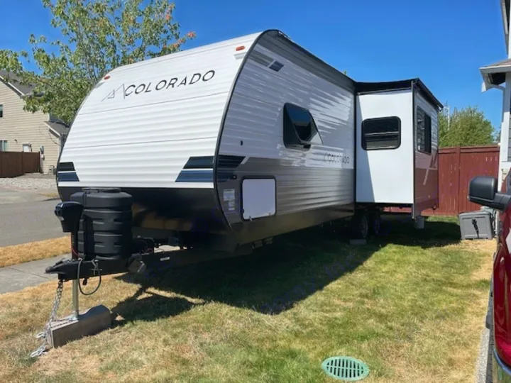 A white Colorado travel trailer RV rental with a slide-out open is ready for adventure, parked on a sunny lawn.. Dutchmen 23RKCWE 2024