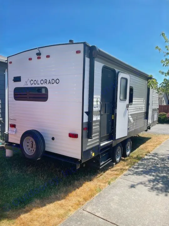 RV rental: This white & gray travel trailer, branded "COLORADO," features an open door & rear spare tire, ready for camping or road trips.. Dutchmen 23RKCWE 2024