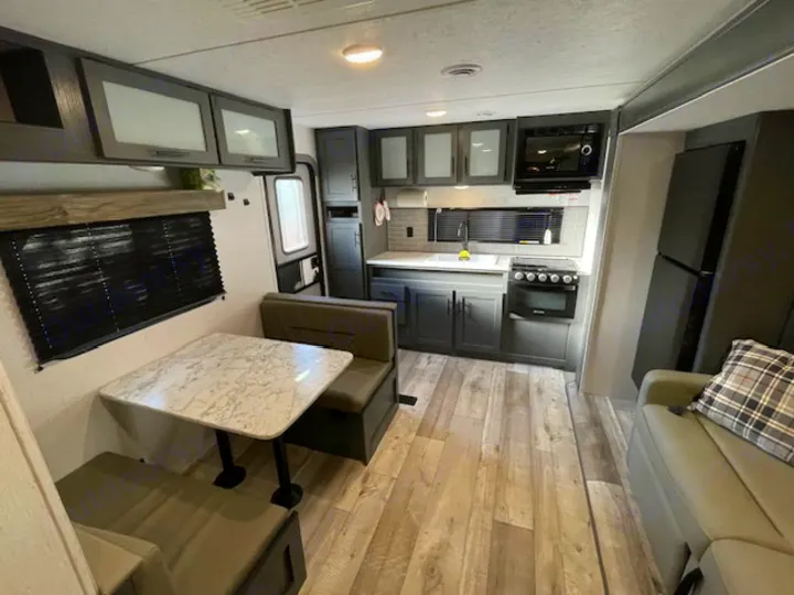 An RV rental's modern interior featuring a kitchen, dining booth, and living area with a sofa and large fridge.. Dutchmen 23RKCWE 2024