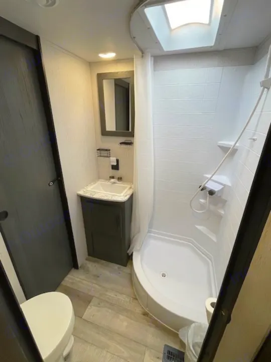 Explore this clean RV rental bathroom with a toilet, sink, and corner shower with a skylight for natural light.. Dutchmen 23RKCWE 2024