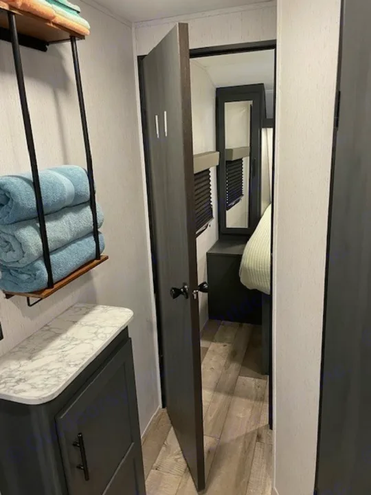 RV rental interior: Bathroom vanity with towels, an open door revealing a cozy bedroom with a bed.. Dutchmen 23RKCWE 2024