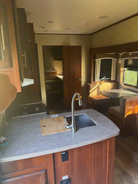 View inside an RV rental, highlighting the kitchen with a sink, stovetop, and a cozy dinette area. A bunk room is visible through the open door.. Jayco Eagle HT 2018