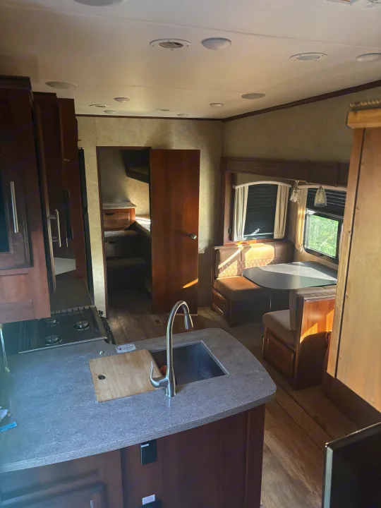 Modern RV rental interior showing kitchen with sink/stove, dining booth, bunk beds, and wood cabinetry throughout.. Jayco Eagle HT 2018