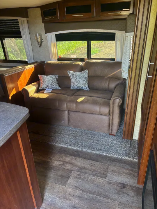 Step into this RV rental's inviting living area: a brown sofa, overhead cabinets, and bright windows showcasing greenery.. Jayco Eagle HT 2018
