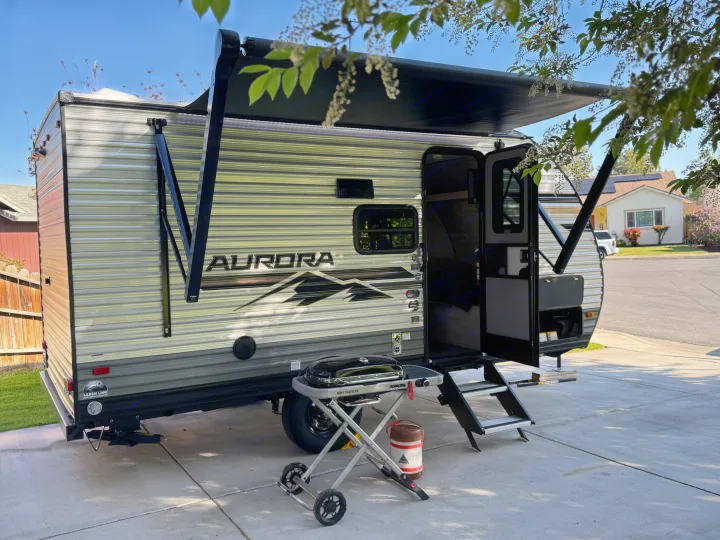 Spacious Aurora travel trailer RV, ideal for an rv rental, with extended awning and portable grill on a sunny day.. Forest river Aurora light 16BHX 2025