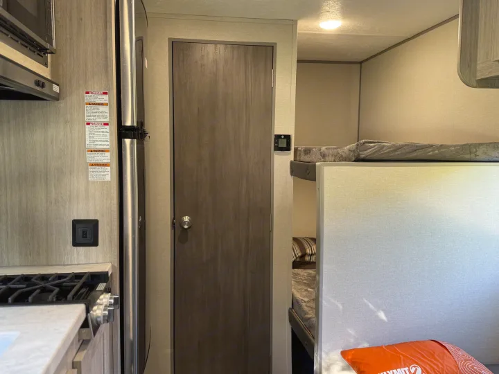Inside an RV rental: kitchen with stove & microwave, refrigerator, door, and cozy bunk beds. Ready for your next adventure.. Forest river Aurora light 16BHX 2025