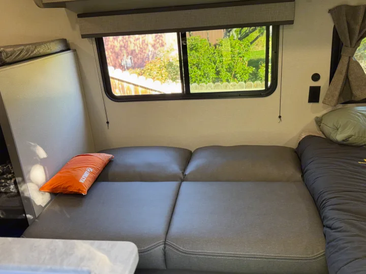 Cozy RV rental interior with grey cushions, Klymit pillow, rolled sleeping bag, and a view outside the window.. Forest river Aurora light 16BHX 2025