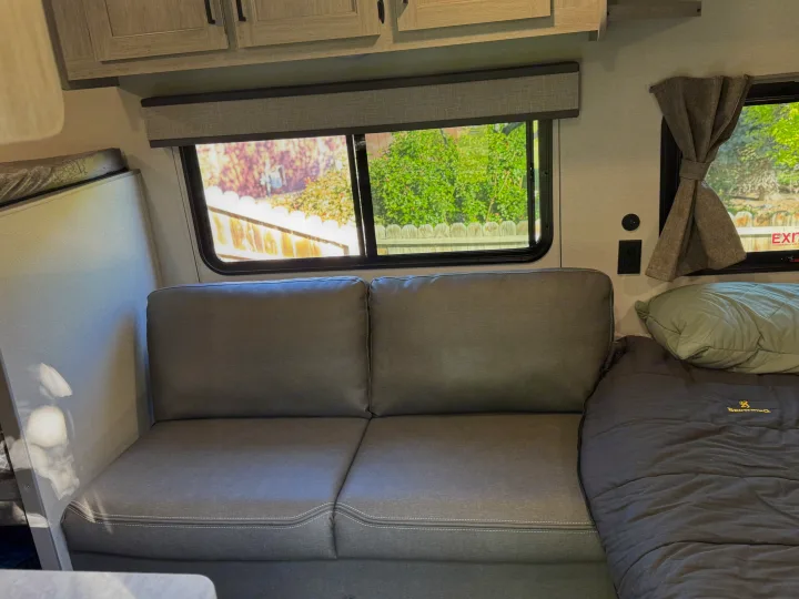 Comfortable RV rental living space featuring a gray sofa, large windows, and an adjacent sleeping bag.. Forest river Aurora light 16BHX 2025