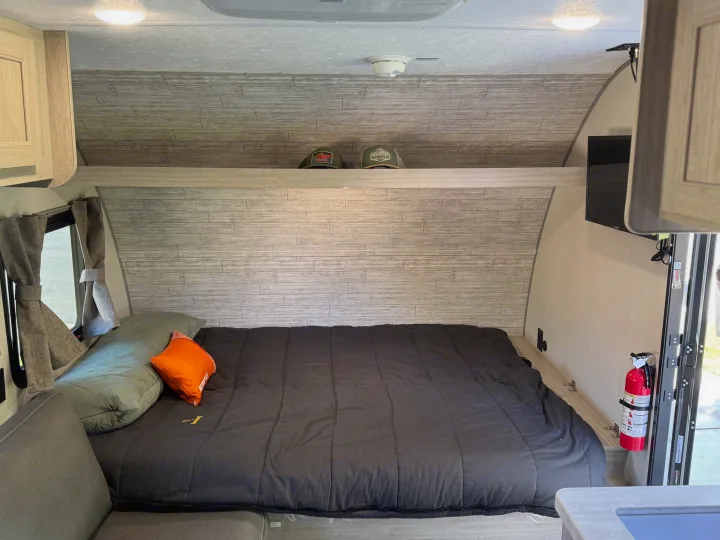 RV rental bedroom featuring a comfortable bed, light wood-look walls, overhead storage, TV, and safety gear.. Forest river Aurora light 16BHX 2025