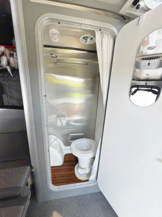 Compact RV rental bathroom: shower, toilet, sink, polished metal walls, and a wooden floor insert.. Airstream Basecamp 2021