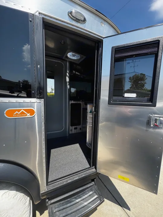 Open door of an Airstream Basecamp RV rental. Its silver exterior and dark interior are visible, ready for adventure.. Airstream Basecamp 2021